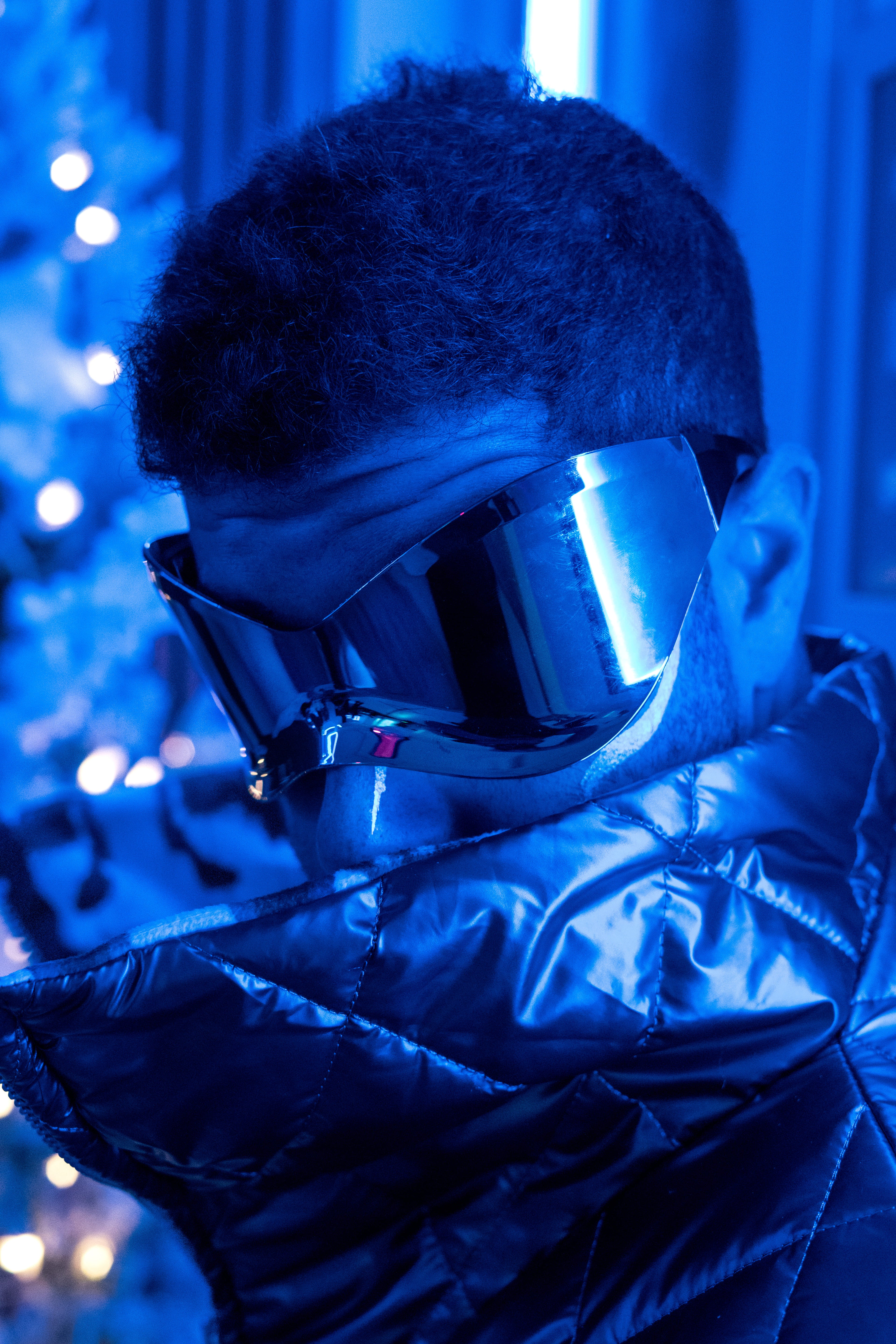 Person wearing big goggles and puffer jacket in a blue-lit setting
