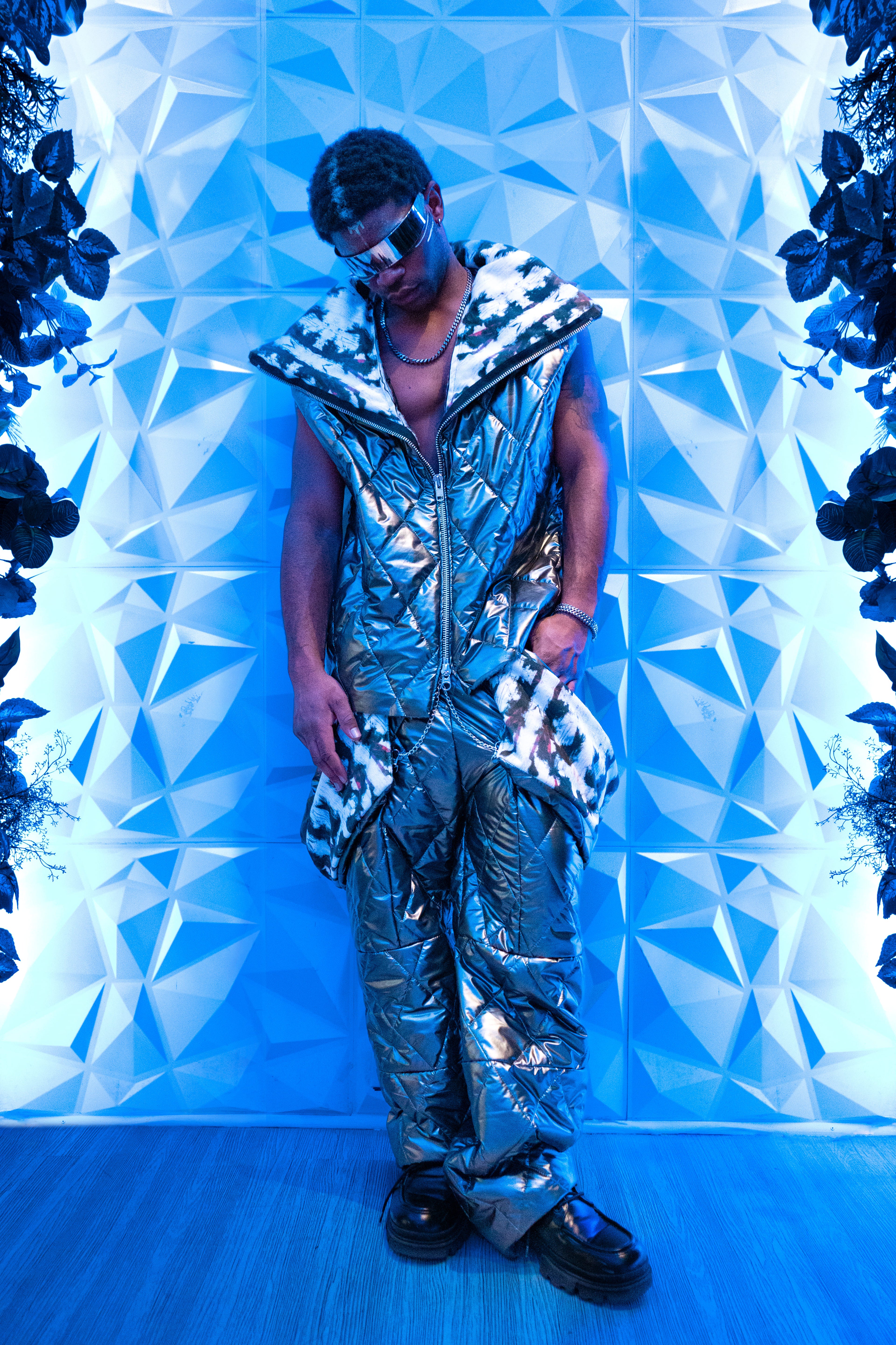 Person wearing a reflective silver outfit against a geometric blue wall.