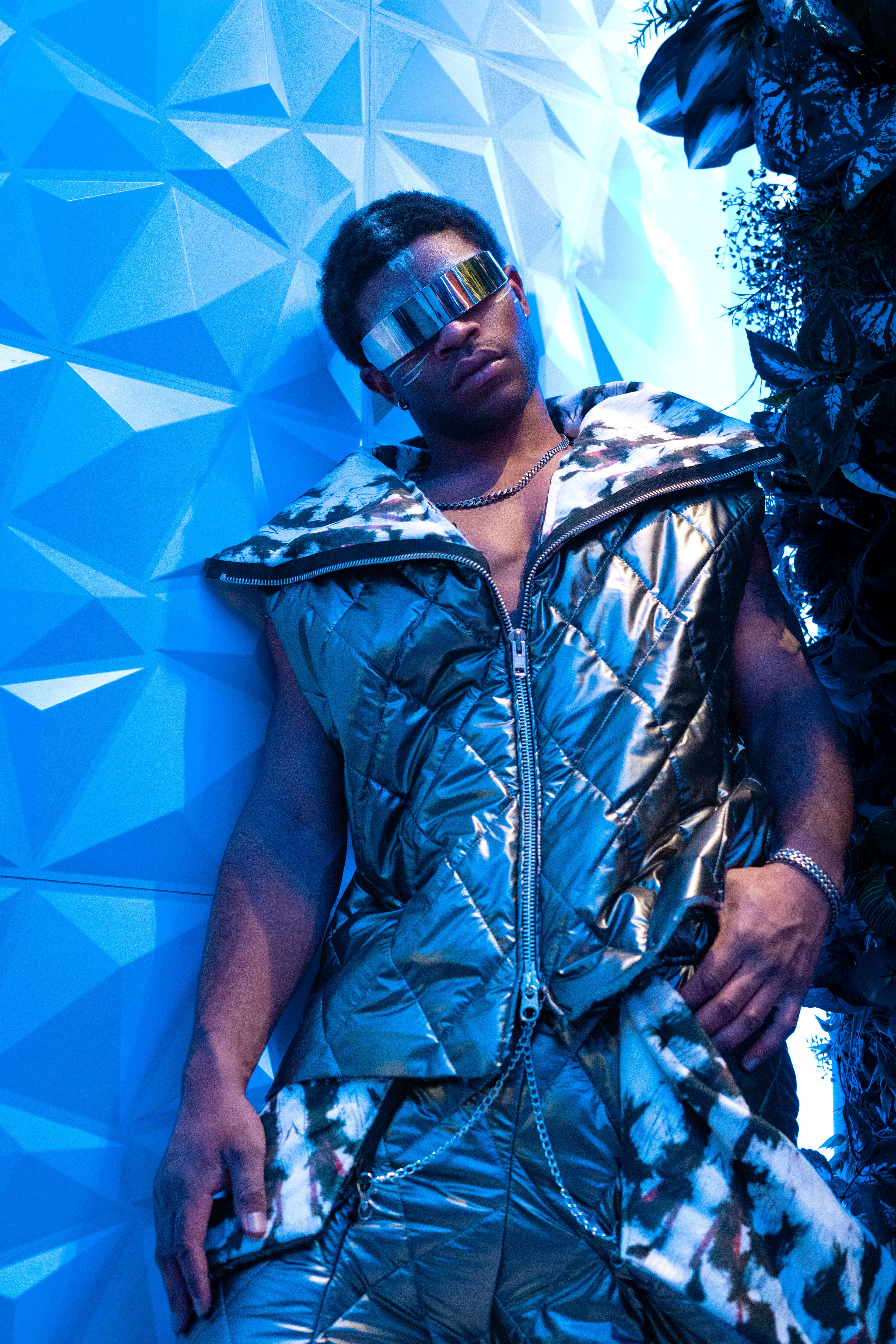 Person wearing a shiny silver outfit against a geometric blue wall.