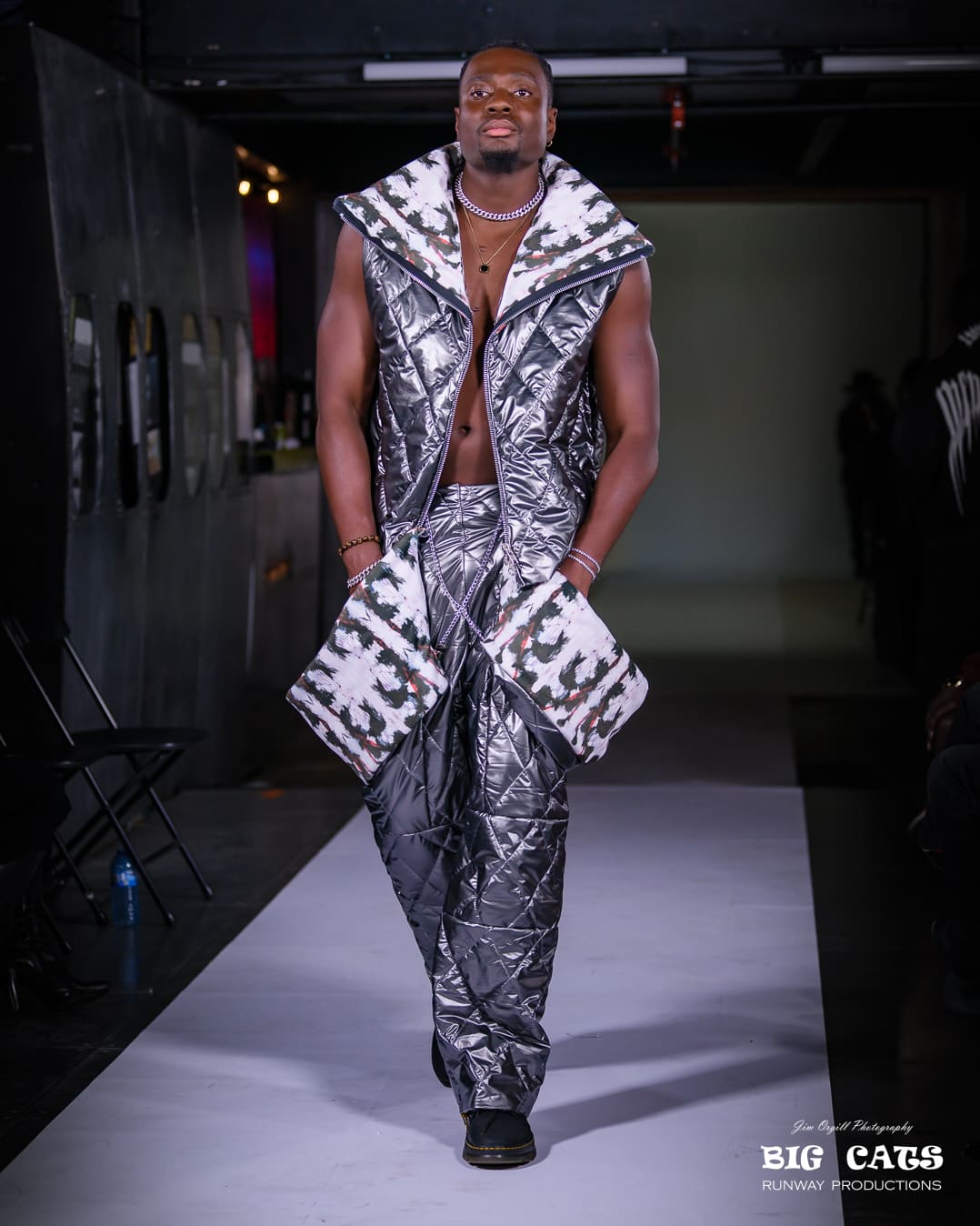 Model wearing a reflective silver outfit on a runway with 'Big Cats' branding.