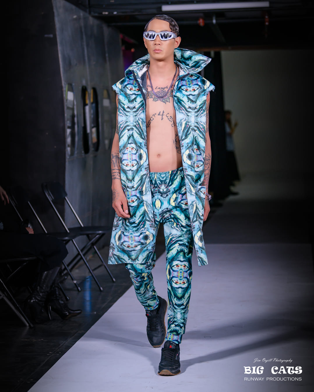 Model wearing a blue patterned outfit on a runway with 'Big Cats' branding.