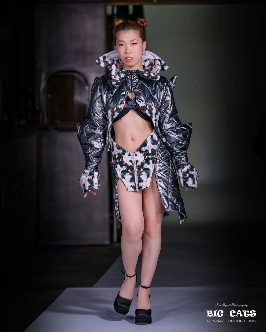 Model walking on a runway wearing a unique outfit with a dark background