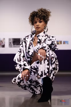 Person wearing a black and white patterned outfit crouching in a studio.