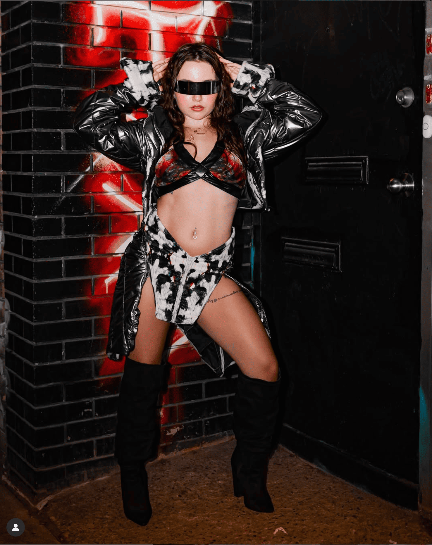 Person in a stylish outfit standing against a brick wall with red accents.