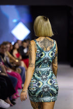 Model walking on a runway wearing a colorful blue, yellow, and black dress with a pattern.