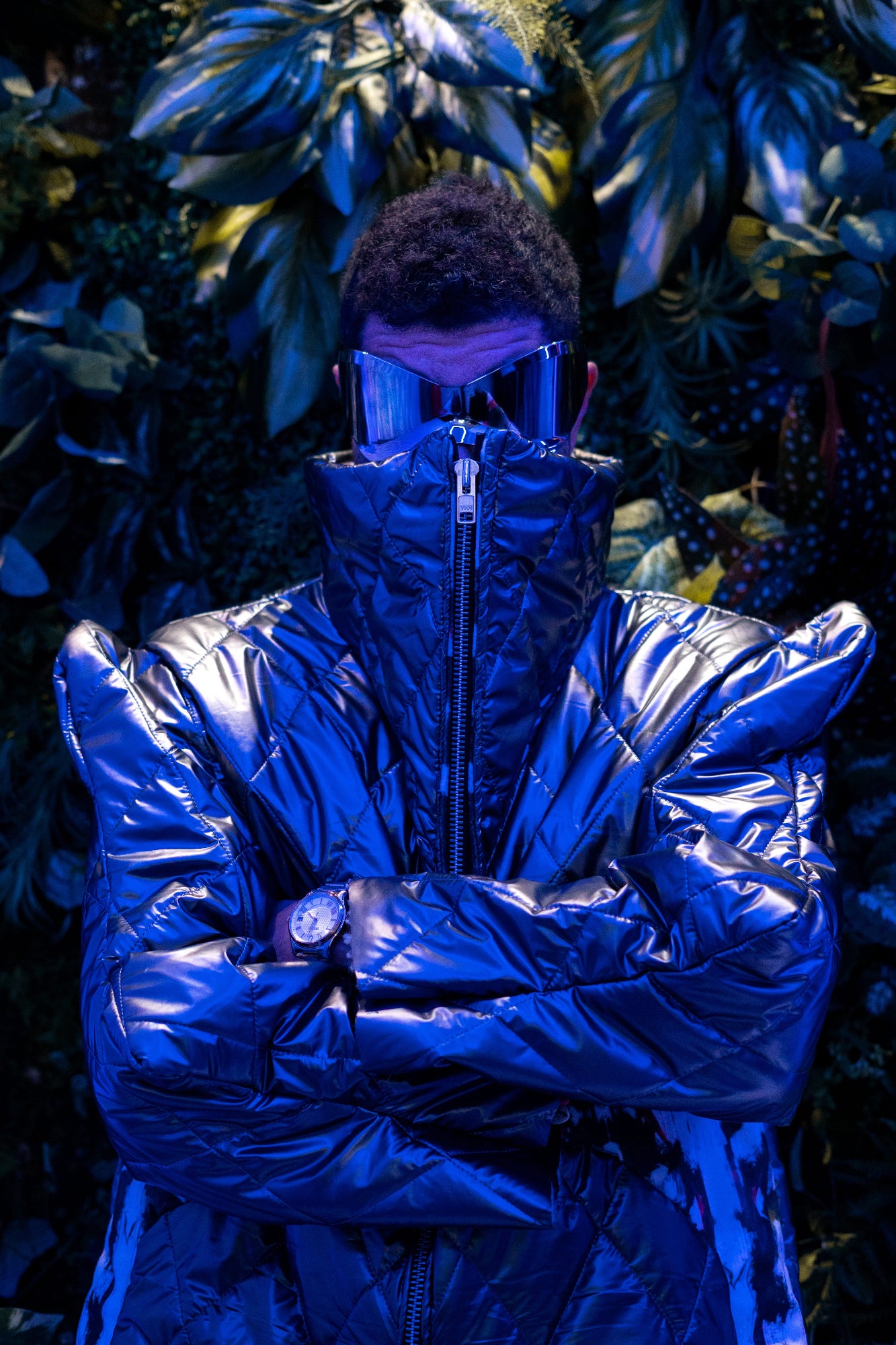Person wearing a reflective blue jacket standing against a dark, leafy background