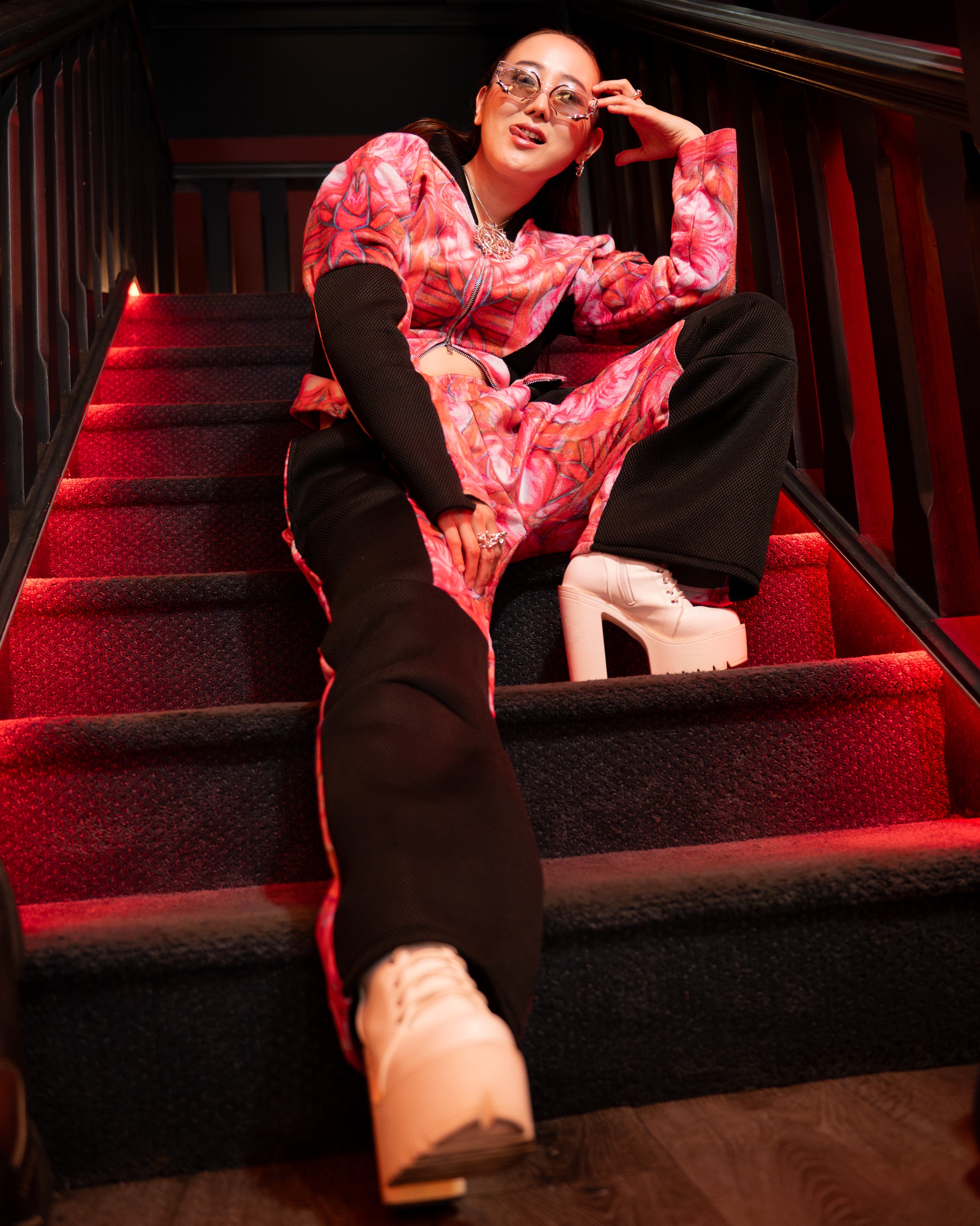 Person in a colorful outfit sitting on red steps with a dark background