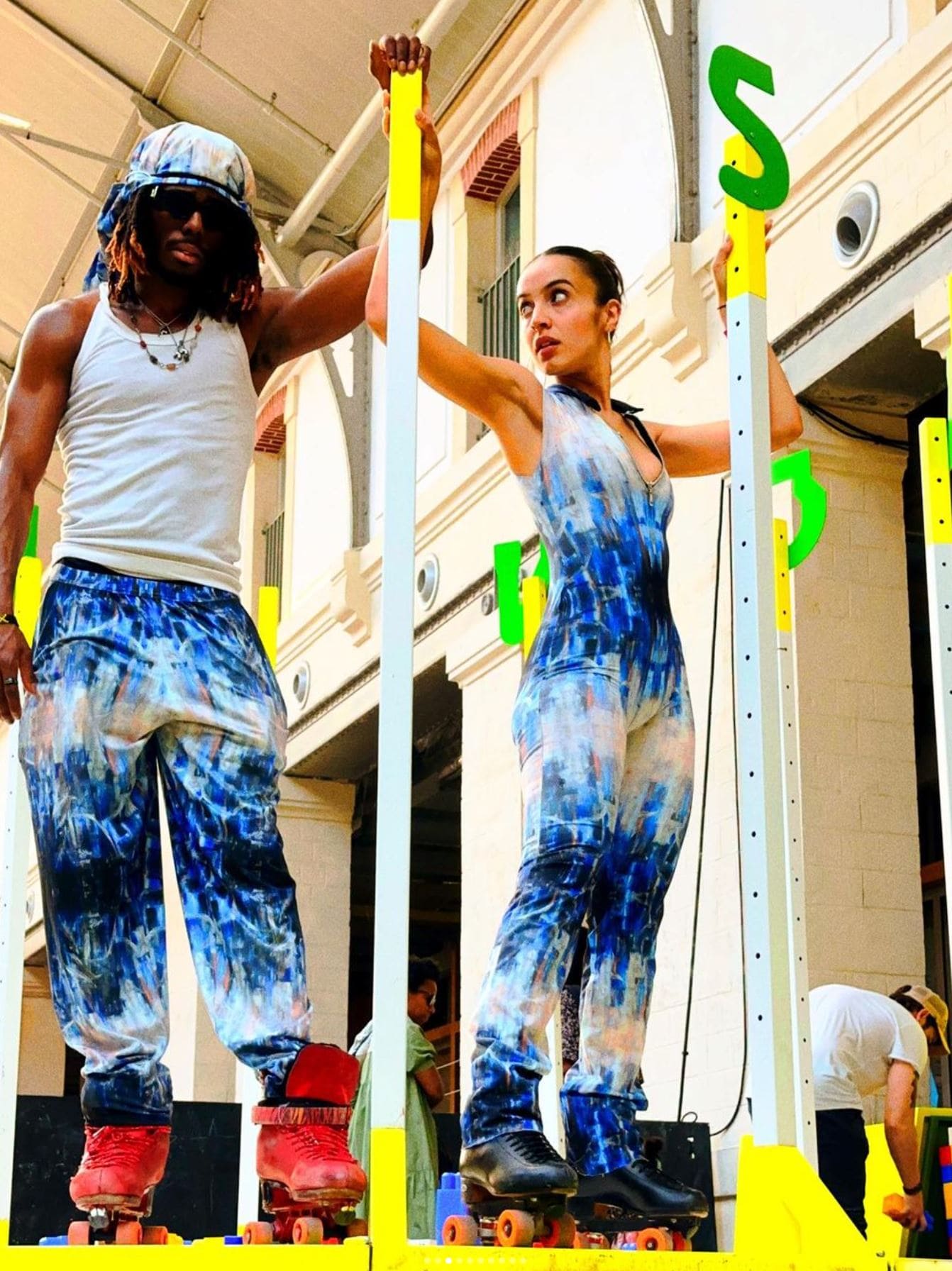 Two people in tie-dye outfits standing on a platform with colorful letters around them.