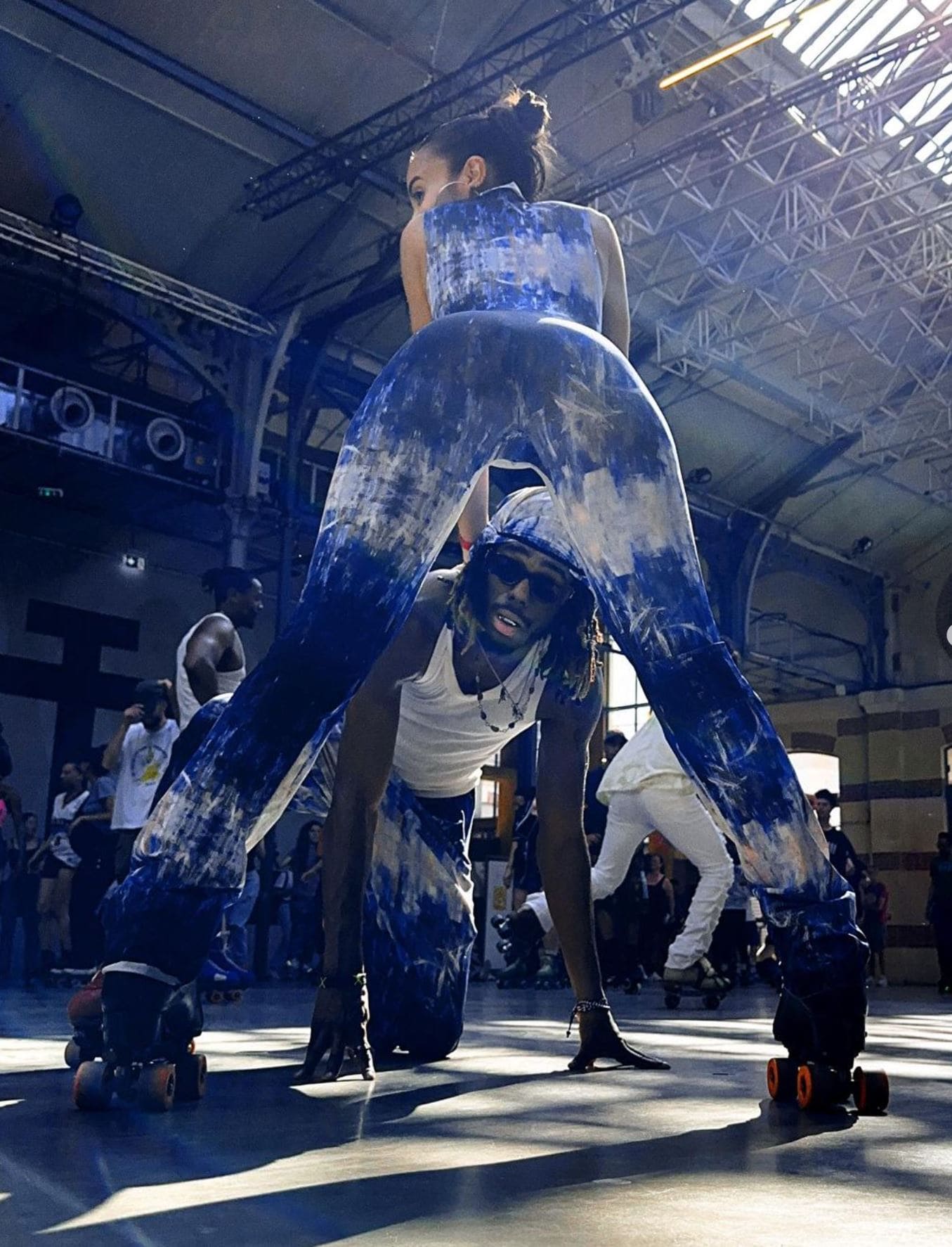 Person in a blue and white dress on roller skates in an indoor setting with people in the background