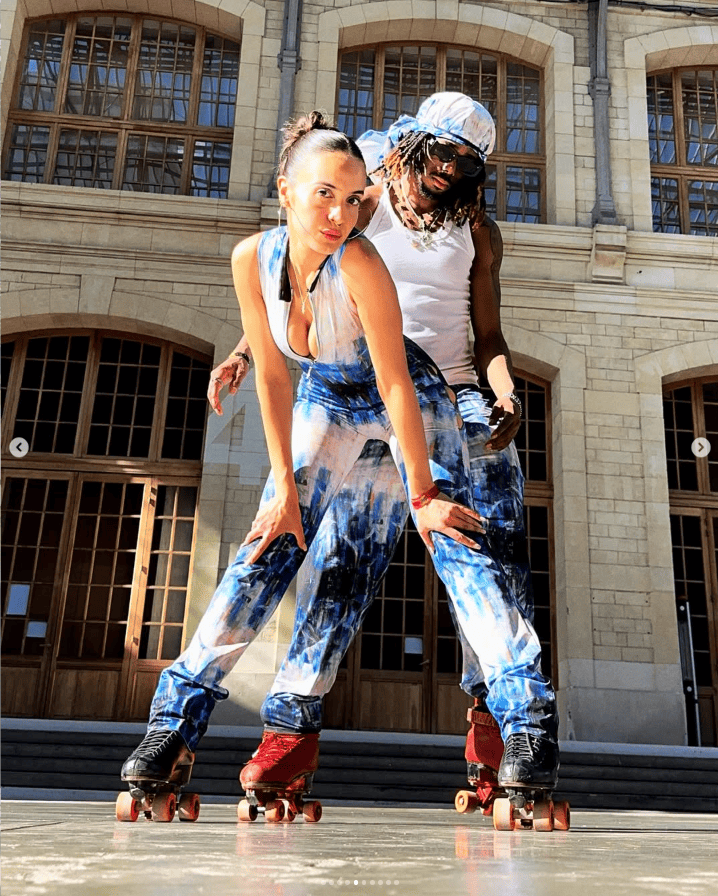 Two people roller skating in front of a large building with arched windows.